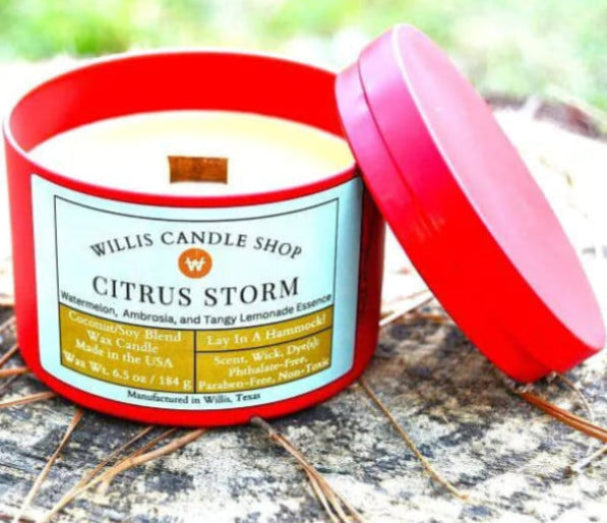 Citrus storm scented candle on log at Willis Candle Shop as red tin candle.