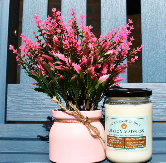 White wax candle with Amazon Madness fragrance next to a vase with flowers.