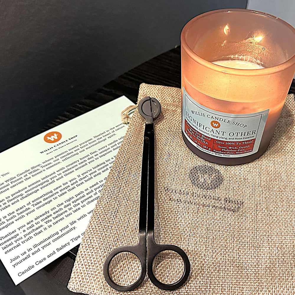 Black frosted scented candle burning by candle care card and candle wick cutters.