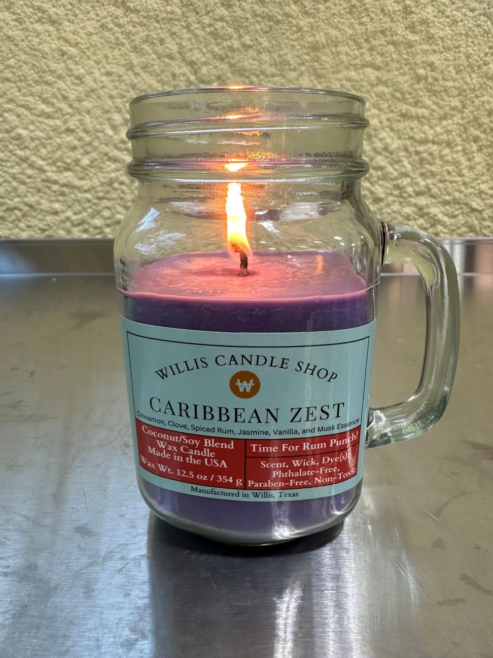 Caribbean Zest candle with burning flame and violet wax at the Willis Candle Shop.