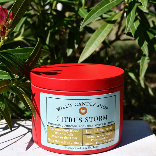 Red tin candle with Citrus Storm scent next to a tree in Willis, Texas.