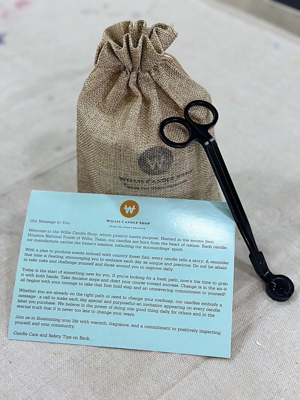 Scented candle in a burlap bag with candle care card and wick trimmers.