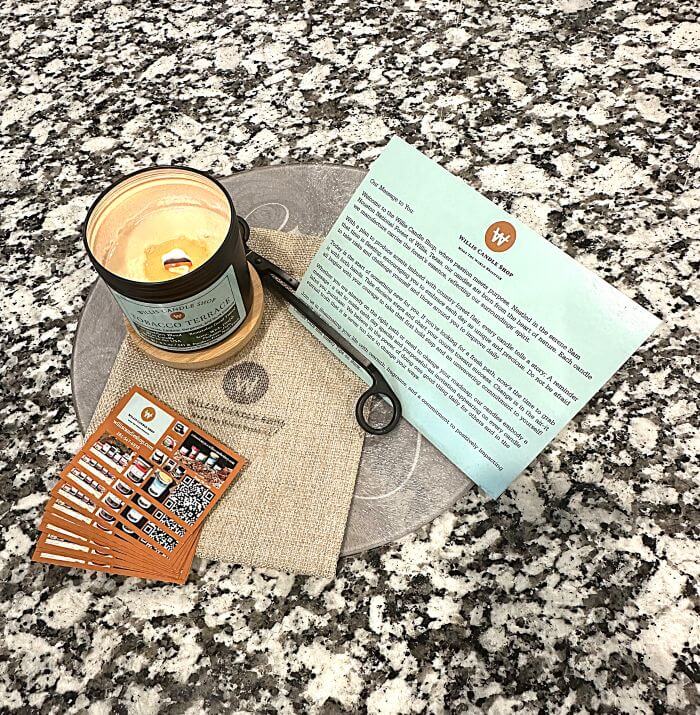 Tobacco candle with candle care card and wick trimmers on burlap bag.