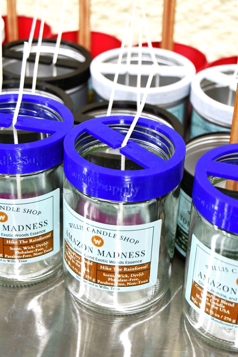 Candle containers staged for wax infiltration with wick holders on glass jars and metal tins.