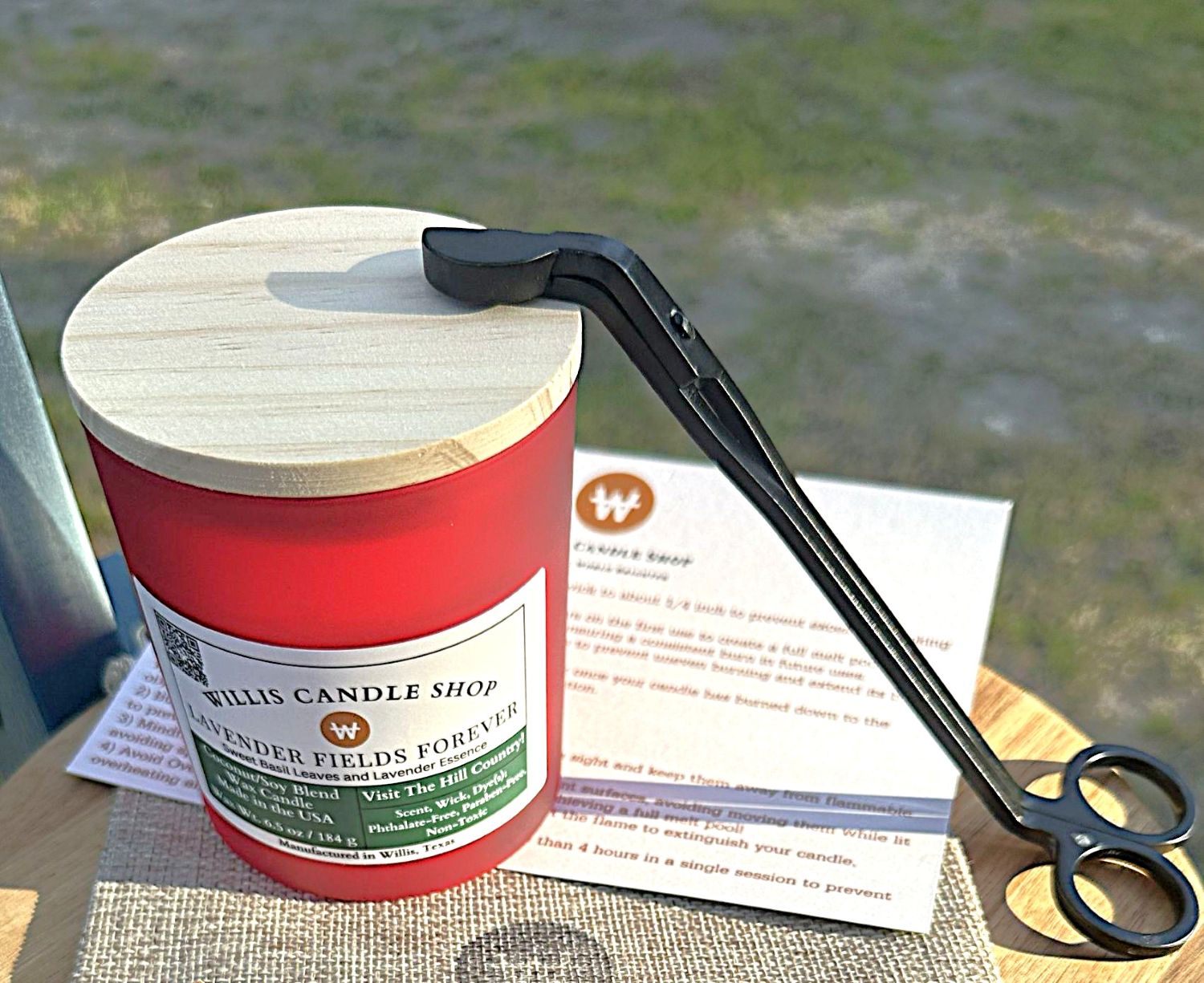 Red candle with wick trimmer and candle care card on a burlap bag in Willis, Texas.