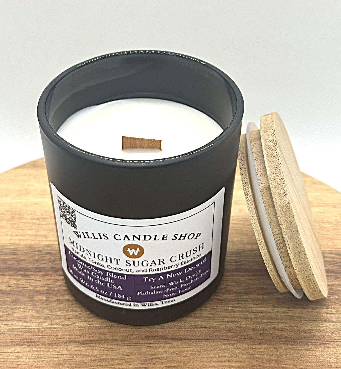 Solid black candle container with wood wick and bamboo lid leaning on container.