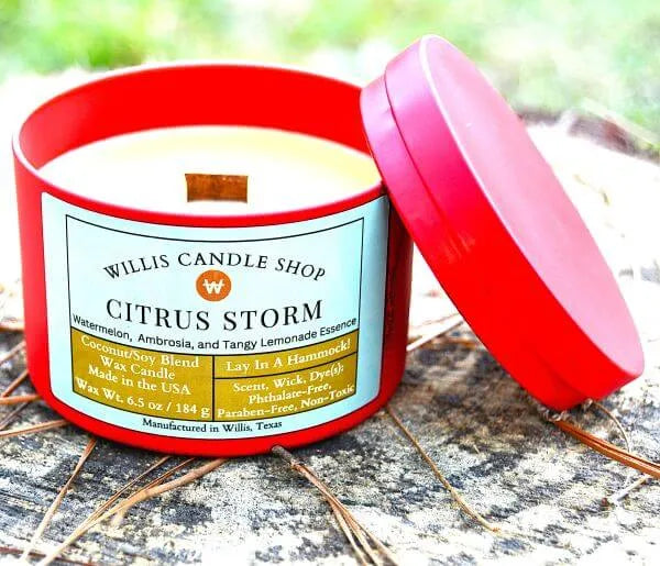 
                  
                    Citrus storm scented candle on log at Willis Candle Shop as red tin candle.
                  
                